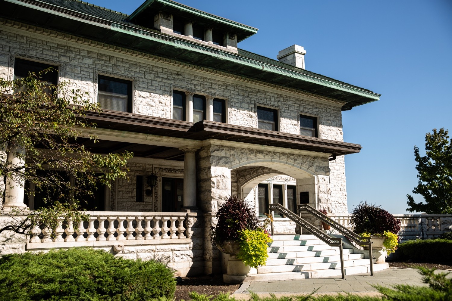 Front view of Piper Hall at Loyola University Chicago, showcasing its stone exterior, columned porch, arched entrance, and landscaped greenery on a clear sunny day.